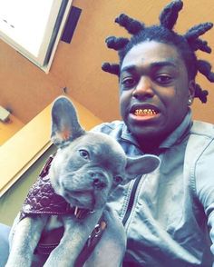 a man with dreadlocks holding a small dog in his lap and looking at the camera