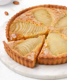 an apple tart on a white plate with almonds around the edges and one slice cut out