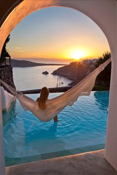 a woman sitting in a hammock next to a swimming pool at sunset with the sun setting