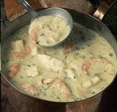 a pot filled with shrimp and cheese on top of a wooden table next to bread