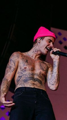 a man with tattoos on his chest holding a microphone and wearing a pink beanie