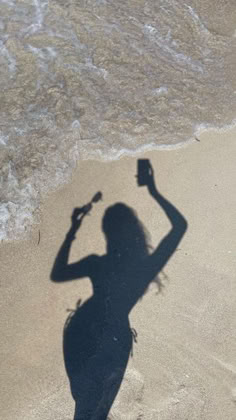 the shadow of a woman on the beach holding a bottle and a cell phone in her hand