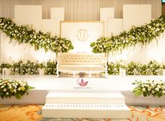 a white couch sitting on top of a stage covered in flowers and greenery next to a wall