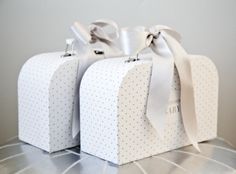 two white boxes with bows on them sitting on a table next to another box that has polka dots