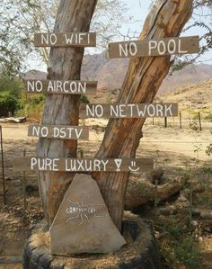 a tree with signs on it in the middle of a desert area that says no wifi, no pool, no aircon, no network, no dsty, no dysy, pure luxury y