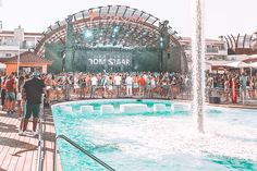 people are standing around in front of the water fountain at an outdoor concert venue, while others look on