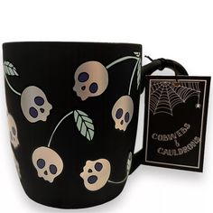 a black coffee mug with skulls and leaves on it, next to a card holder