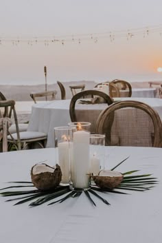 two candles sitting on top of a white table next to some palm leaves and coconuts