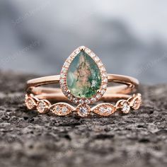 two gold rings with green and white stone in them on top of a rocky surface