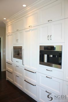 a kitchen with white cabinets and stainless steel ovens in the wall, along with dark wood flooring