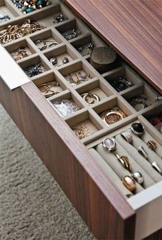 a drawer filled with lots of jewelry on top of a carpeted floor next to a wooden table