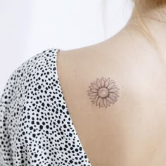 the back of a woman's shoulder with a small sunflower tattoo on it