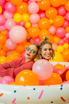 two girls in a tub with balloons and confetti on the wall behind them