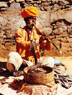 a man in an orange turban is holding a snake while sitting on the ground