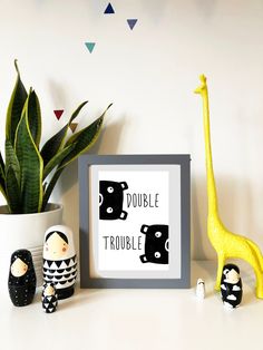 there is a giraffe and two little dolls next to a framed print that says double trouble