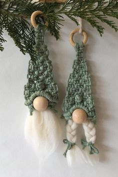 two crocheted gnome ornaments hanging from a tree branch on a white surface with pine needles