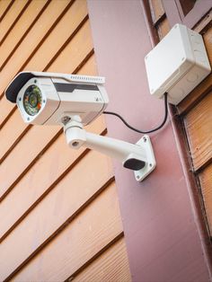 a security camera mounted on the side of a building next to a pink wooden wall