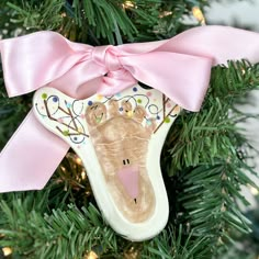 a christmas ornament with a handprint on it and a pink bow hanging from the tree