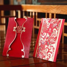 two red and gold cards sitting on top of a wooden table next to each other