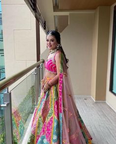 a woman in a pink and green lehenga standing on a balcony