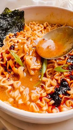 a white bowl filled with noodles and sauce on top of a table next to a spoon