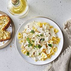 a plate of pasta with bread on the side and a glass of wine next to it