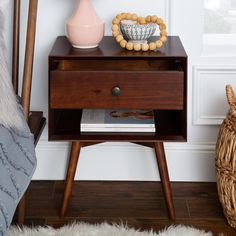 a nightstand with books and candles on it next to a bed in a room that has white walls