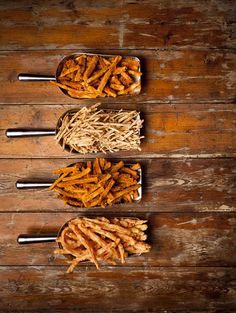 four wooden spoons filled with food on top of a wooden table next to straw