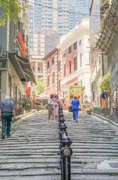 people are walking down the street in an urban area with tall buildings and stone steps