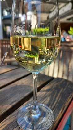 a glass of white wine sitting on top of a wooden table