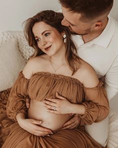 a pregnant woman sitting on top of a bed next to her husband