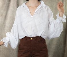 Become your own historical drama with the Darcy Shirt– a garment that channels the charm and refined demeanor of literature's most beloved gentleman. Much like Mr. Darcy, this antique ivory poet blouse exudes a quiet sophistication. It's crafted from 100% cotton with a textured gauze feel, offering comfort that befits a true English gentleman. The dramatic, billowing sleeves, inspired by historical men's undershirts, add a touch of mystery, and the unique knotted button closures at the neckline Astarion Cosplay, Sorbet Shark, Medieval Tunic, Yellow Corset, Wedding Corset, Poet Blouse, Brown Corset, Poet Shirt, Corset Shop