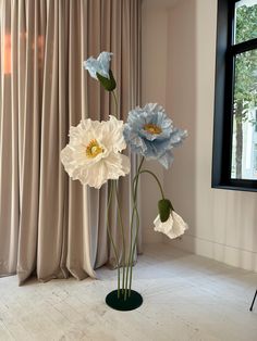 three white and blue flowers are in a vase on the floor next to a window