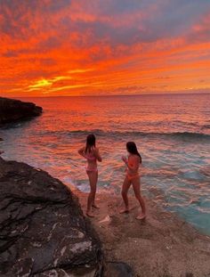 two women in bathing suits standing on the rocks near the ocean at sunset or sunrise