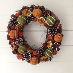 a wreath made out of fruit and pine cones is hanging on a white wooden wall