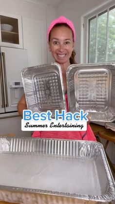 a woman is holding up two trays of labor day bbq food in her kitchen