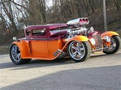 an orange and red hot rod car parked on the side of the road in front of some trees