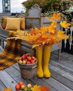 a wooden deck with fall leaves, apples and yellow boots