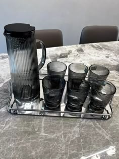 a glass pitcher and six glasses on a tray with marble table top in the background