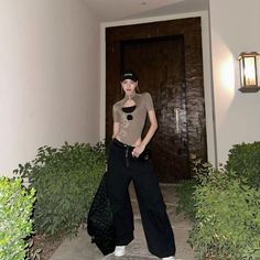 a woman standing in front of a door with her hand on her hip while wearing black pants