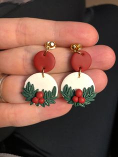 a pair of red and white earrings with holly leaves