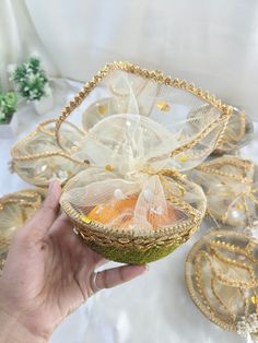 a hand holding a basket filled with fruit on top of a white cloth covered table