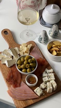 a wooden cutting board topped with lots of food next to glasses of wine and cheese