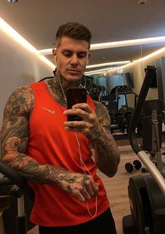 a man with tattoos on his arm is looking at his cell phone in the gym