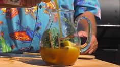 a person pours orange juice into a pitcher filled with green plants and lemons