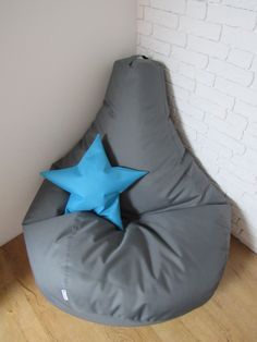 a grey bean bag chair with a blue star on the top and bottom, in front of a white brick wall