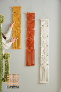 a woman standing in front of three macrame wall hangings on the wall