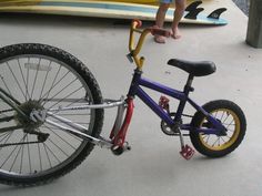 a small child standing next to a purple bike with yellow spokes on the front wheel