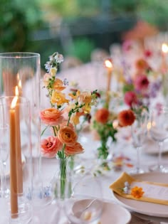 the table is set with candles and flowers in vases, plates and napkins