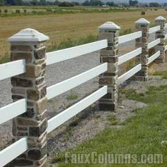 a white fence with stone pillars and posts in front of an open field on a sunny day